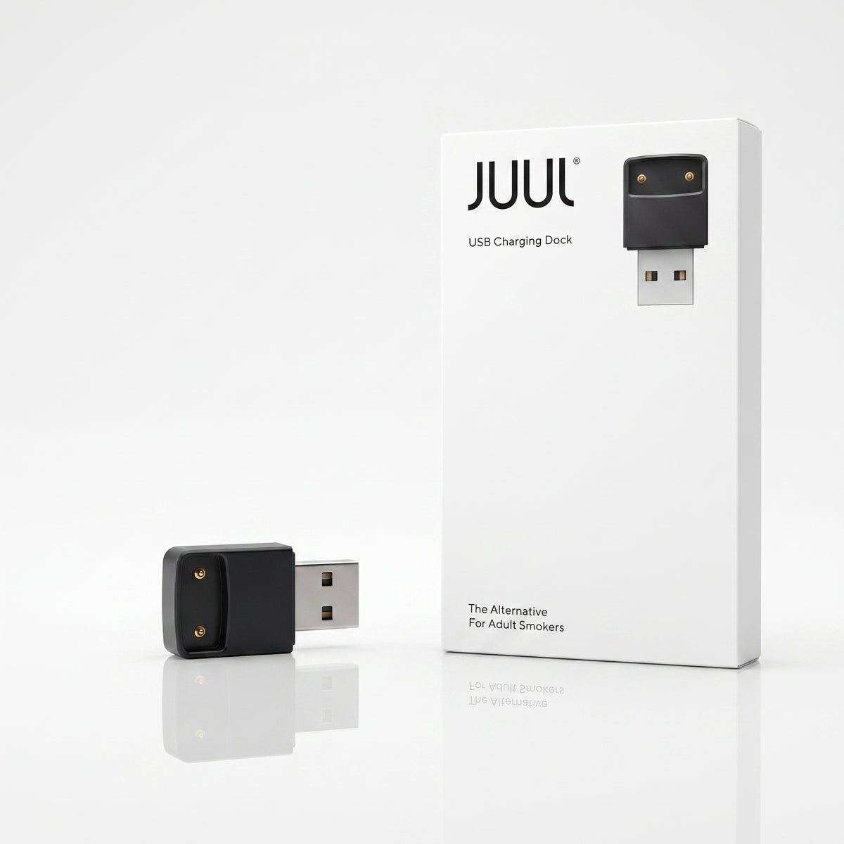 A JUUL USB charging dock shown next to its white retail box on a clean white background. The dock itself is black with two gold-tone contact points and a silver USB connector.