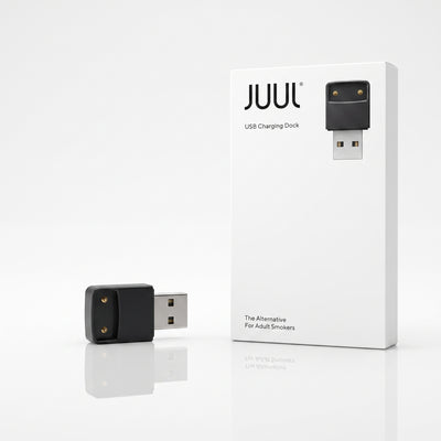 A JUUL USB charging dock shown next to its white retail box on a clean white background. The dock itself is black with two gold-tone contact points and a silver USB connector.