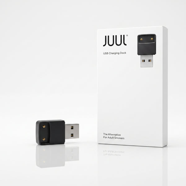 A JUUL USB charging dock shown next to its white retail box on a clean white background. The dock itself is black with two gold-tone contact points and a silver USB connector.